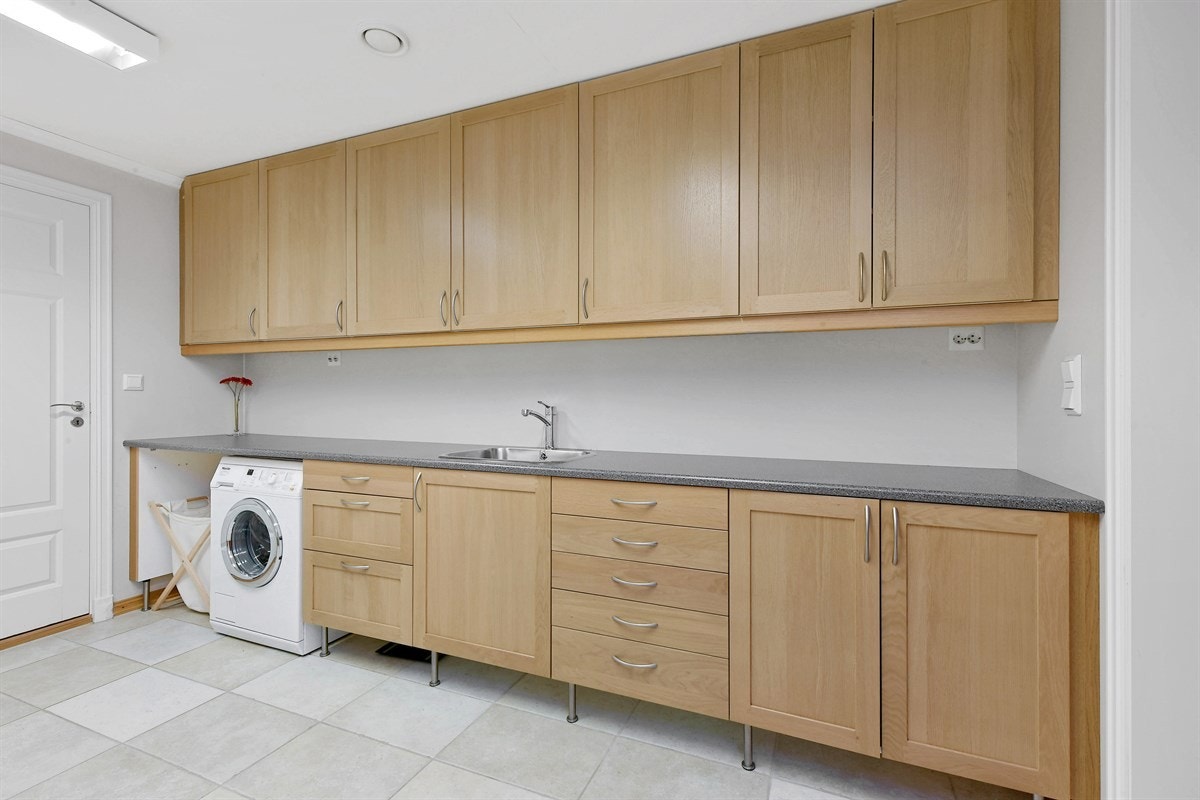 Eneboligen har et stort vaskerom i underetasjen med fliser på gulv, malte vegger, sluk og gulvvarme. Galleribilde