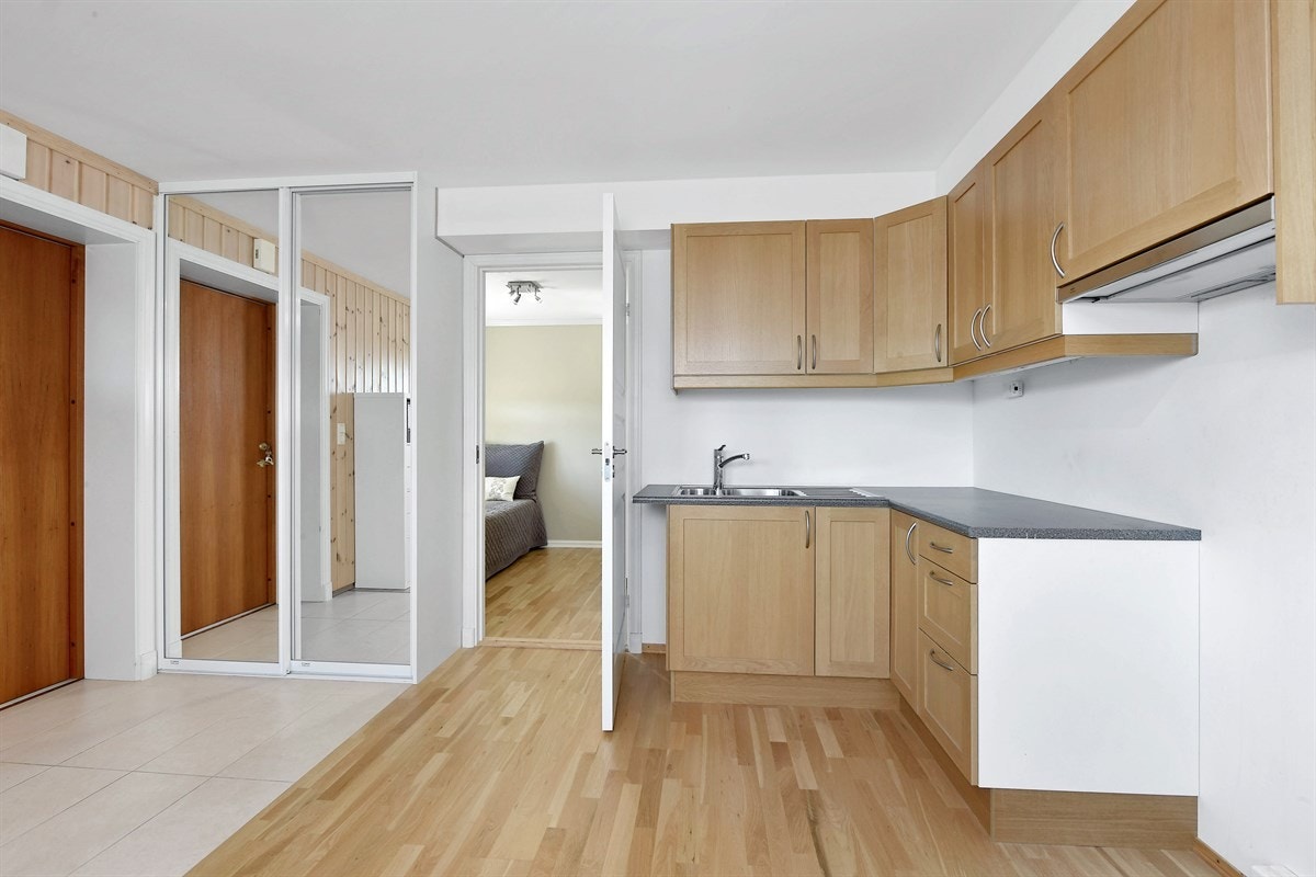 Stuen i hybelen har en åpen kjøkkenløsning langs to vegger med nisje for komfyr og ventilator over kokesonen. Galleribilde