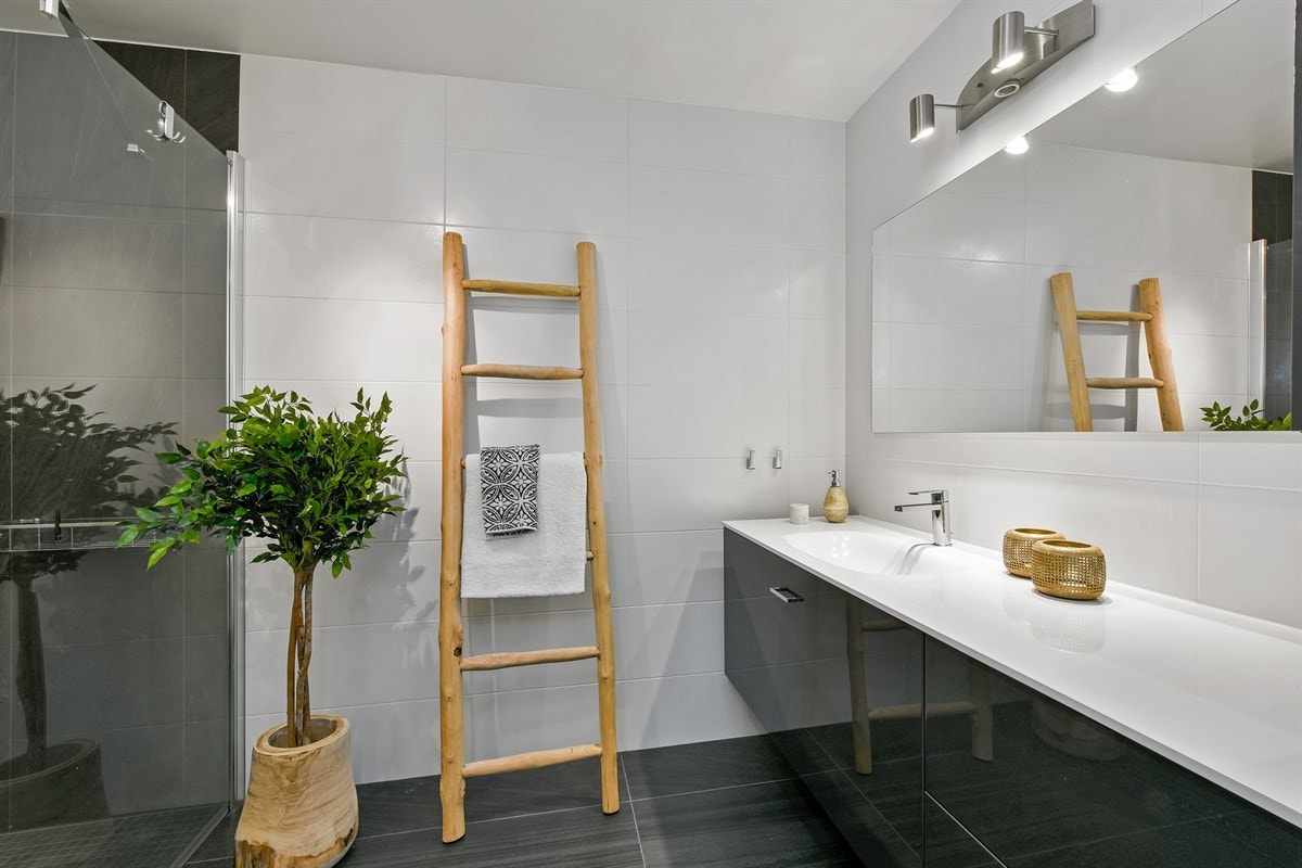 Badet har store grå fliser på gulv, gulvvarme og hvite fliser på veggene. Galleribilde