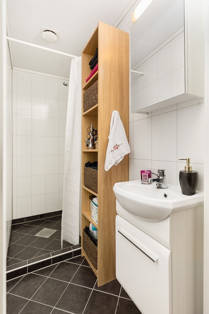 Badet har mørke fliser på gulv, lyse fliser på vegger, gulvvarme og speilbelysning. Rommet har også dusjhjørne, speilskap og en heldekkende servant med underskap Galleribilde