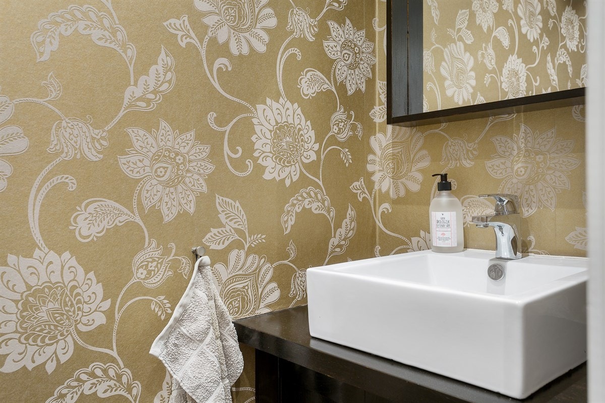 Separat WC med flislagt gulv, tapet på vegger og heltre innredning med vask. Galleribilde