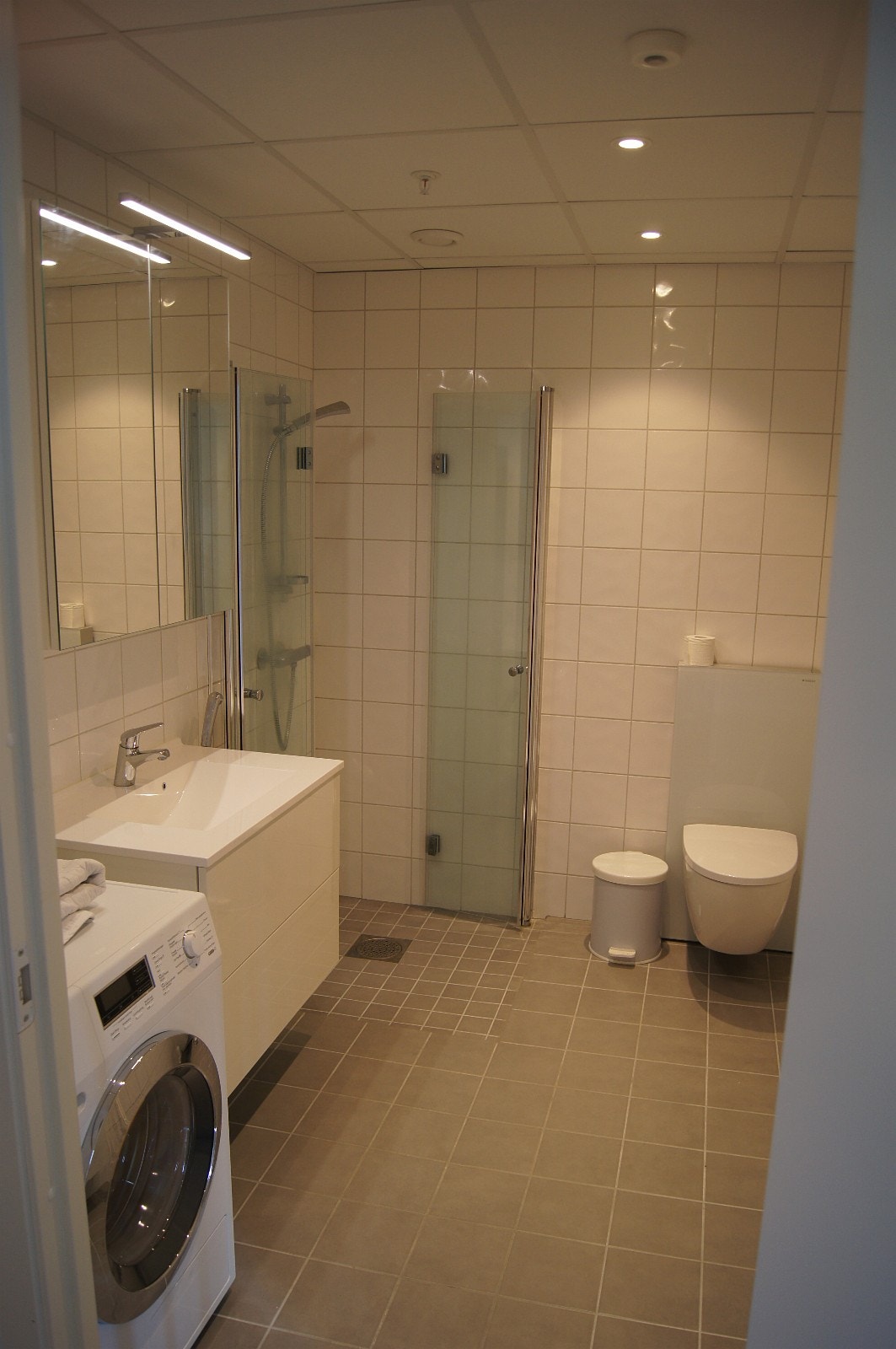 Flislagt bad med speilskap, høgskap og skuffer under servant Galleribilde