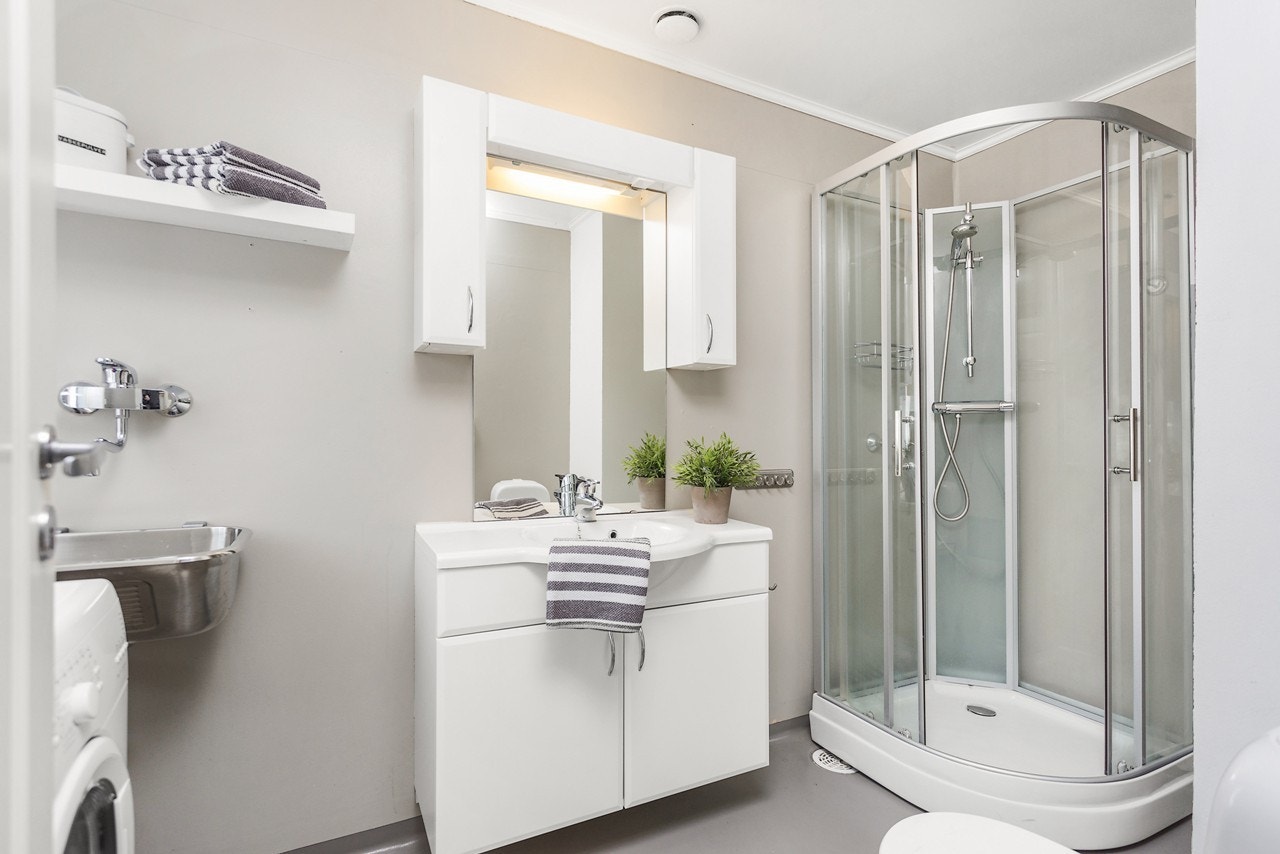 Leilighetens bad er videre utstyrt med et praktisk dusjkabinett som bidrar til direkte avrenning i sluk. Du har også et romslig servantskap med godt med oppbevaringplass i over- og underskap Galleribilde