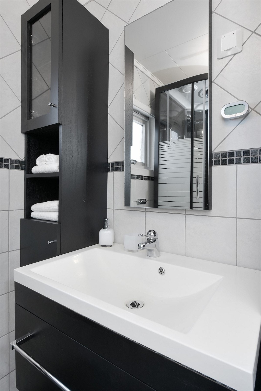 Baderomsinnredningen har mørke fronter og vitrinedører, i tillegg til helstøpt servant over skuffeseksjon. Galleribilde