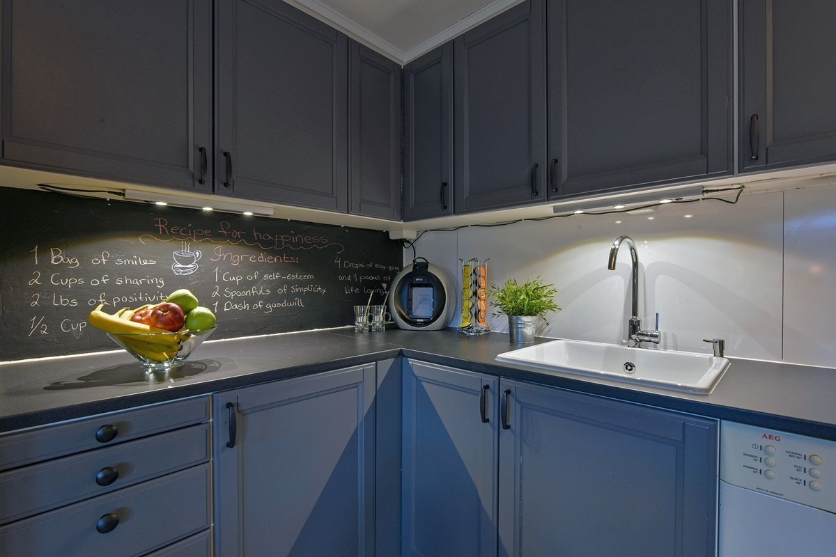 Det er belysning og stålplate over kjøkkenbenk, laminert benkeplate med enkel vaskekum og nisje for kjøleskap. Galleribilde