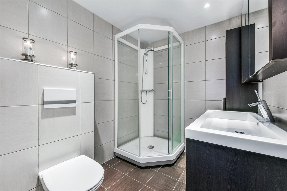 Badet er modernisert i 2013 og fremstår som lyst og delikat. Rommet er utstyrt med downlights i himling, brune fliser på gulv og lysegrå fliser på vegg. Galleribilde