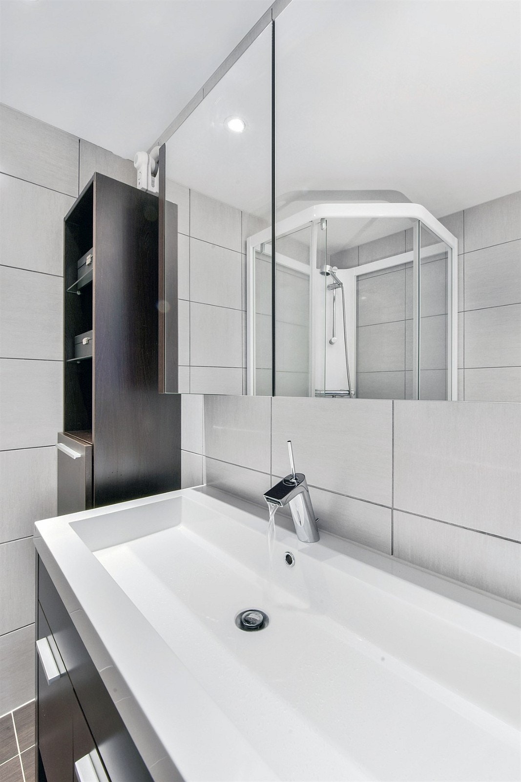 Innredningen består av heldekkende servant, mørkebrun servantmøblement, veggskap, speilskap, veggmontert toalett og dusjkabinett. Galleribilde