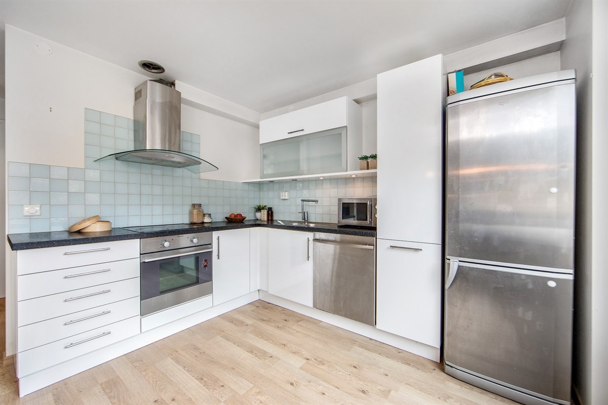 Kjøkkeninnredning fra 2008/2009 med profilerte malte fronter, laminat benkeplate og rustfri nedfelt kum. Fliser på vegg over benk og ventilator tilsluttet kanal. Integrert platetopp, stekeovn og oppvaskmaskin. Galleribilde