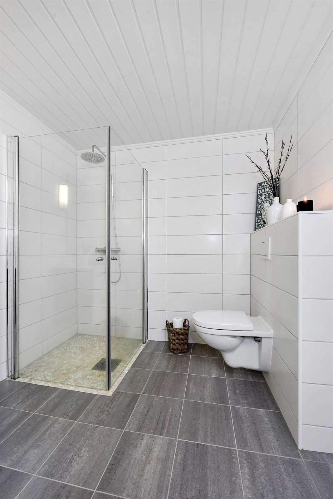 Rommet har grå fliser på gulv med gulvvarme, hvite fliser på veggene og hvitmalt panelhimling. Galleribilde