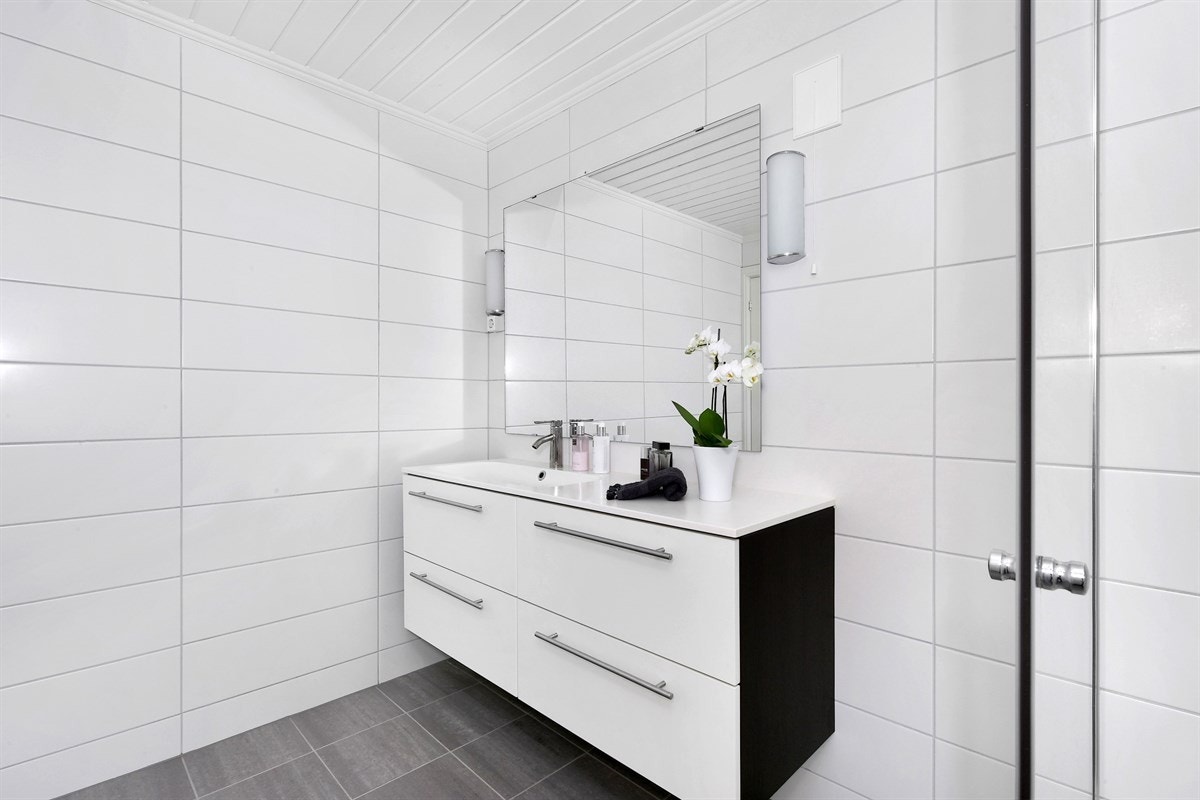 Innredningen består av heldekkende servantplate på lys skuffeseksjon, speil med sidebelysning, samt en flott dusjnisje med rullesteinsgulv, innfellbare glassdører og regnfallsdusj. Galleribilde