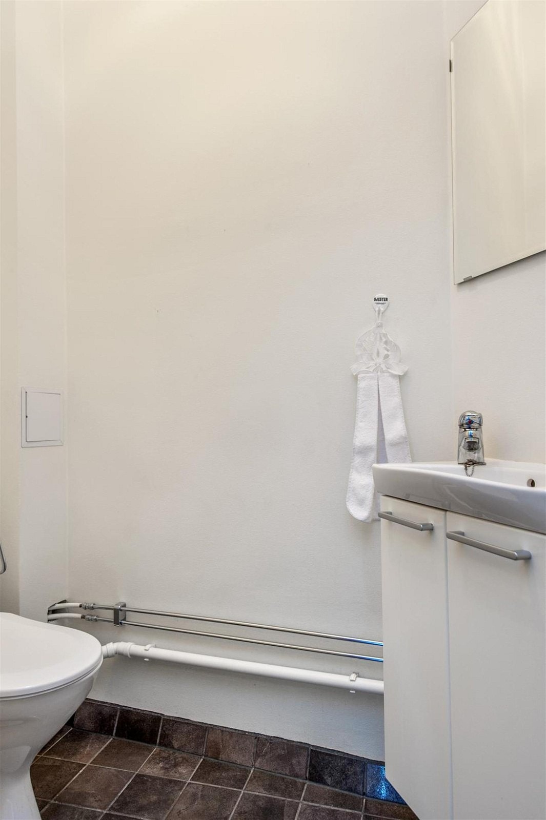 WC med fliser på gulv, klosett og servant med underskap. Galleribilde