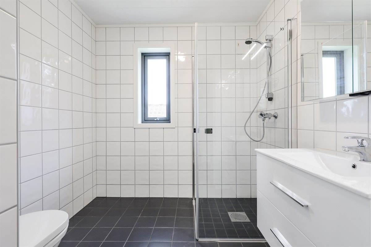Bad med veggmontert toalett, dusjhjørne med glassdører. Galleribilde