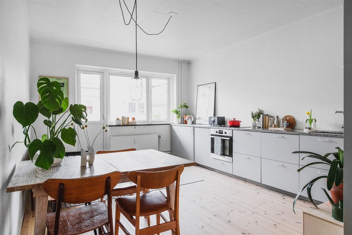 Det kombinerte rommet med stue og kjøkken utgjør i dag et naturlig tyngdepunkt i leilighetens gjennomgående romløsning og er et fullkomment sosialt samlingsrom for både hverdagslig opphold og matlaging. Galleribilde