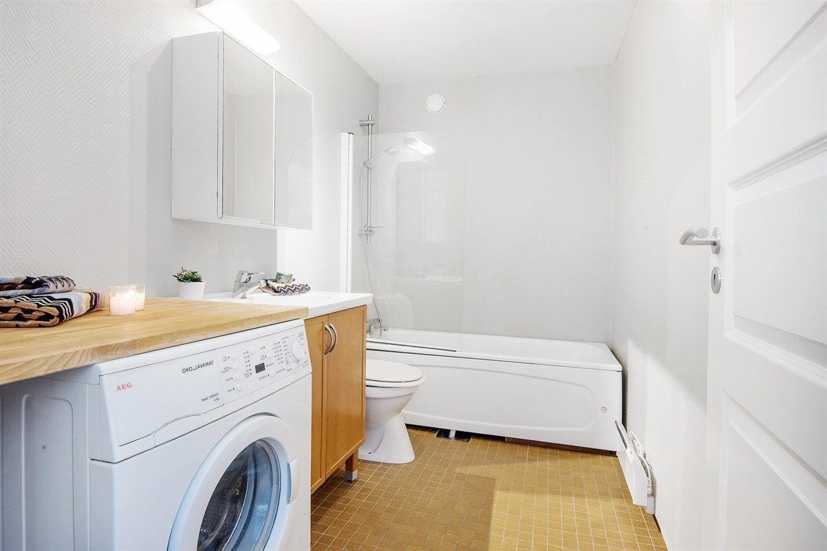 Bad med fliser, badekar og opplegg for vaskemaskin. Galleribilde