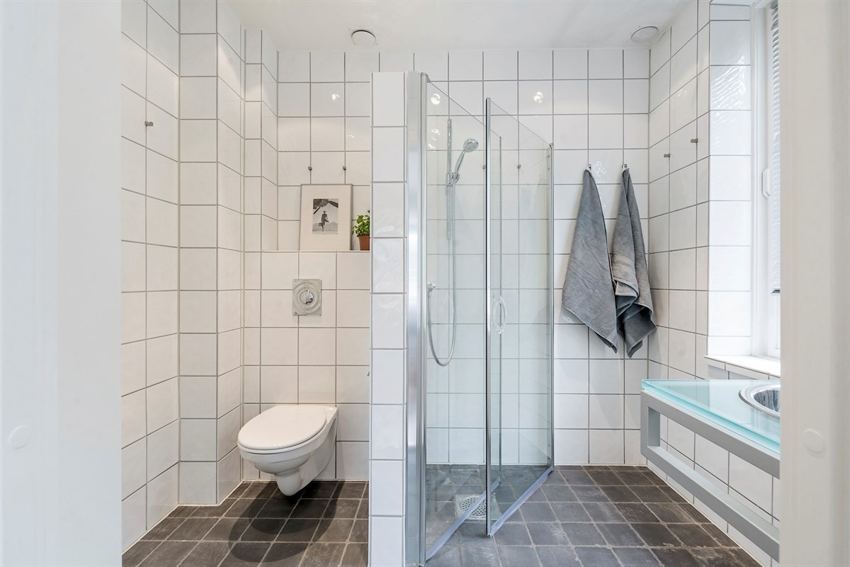 Badet er utstyrt med downlights i himling, mørke fliser på gulv og lyse fliser på vegg. Varmekabler i gulv Galleribilde
