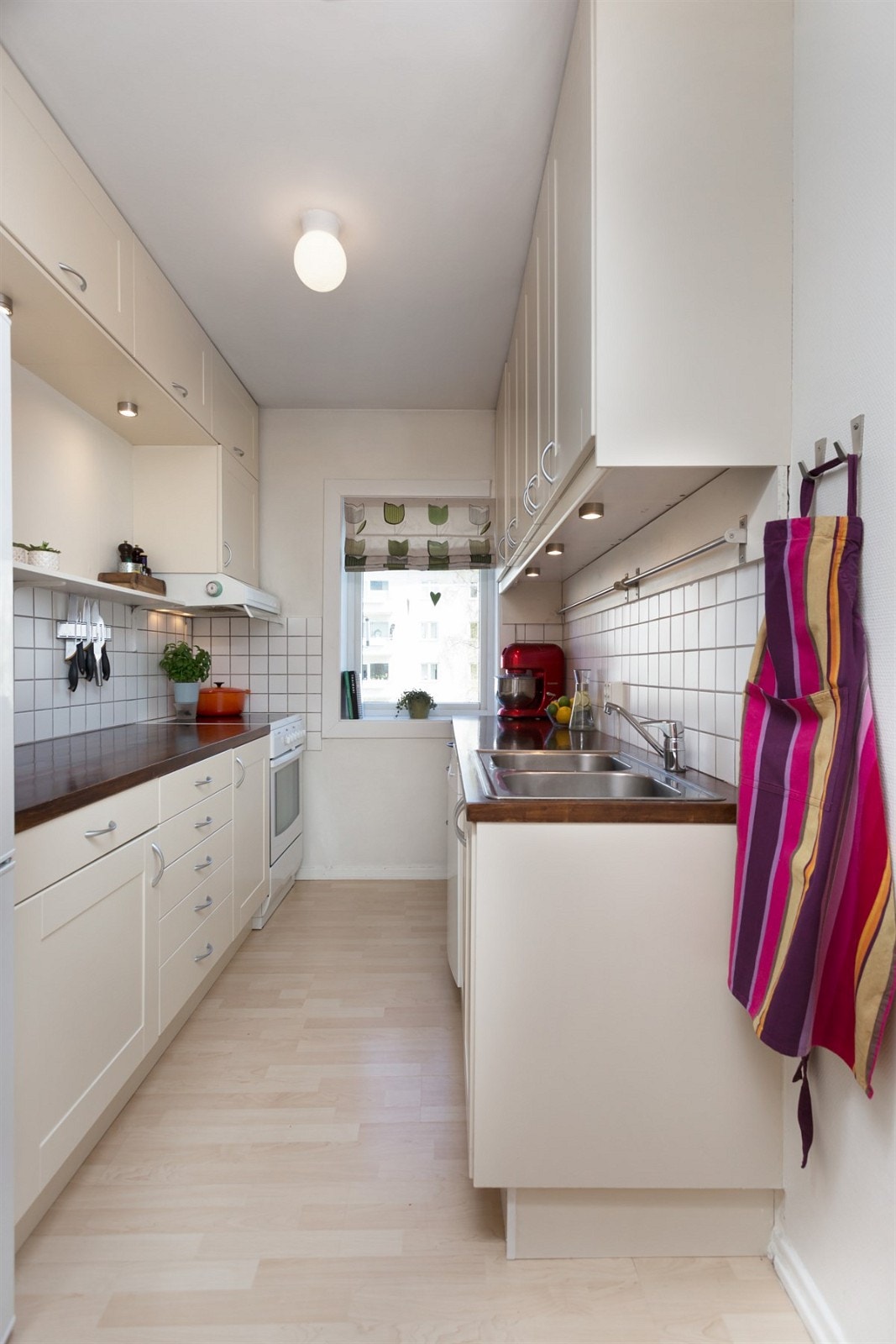 Kjøkkeninnredning med beige profilerte fronter, benkeplate i heltre med nedfelt kum og ett-greps blandebatteri, fliser i sprut sone. Hvitevarer som komfyr, oppvaskmaskin og ventilator som er plassert i skap. Galleribilde