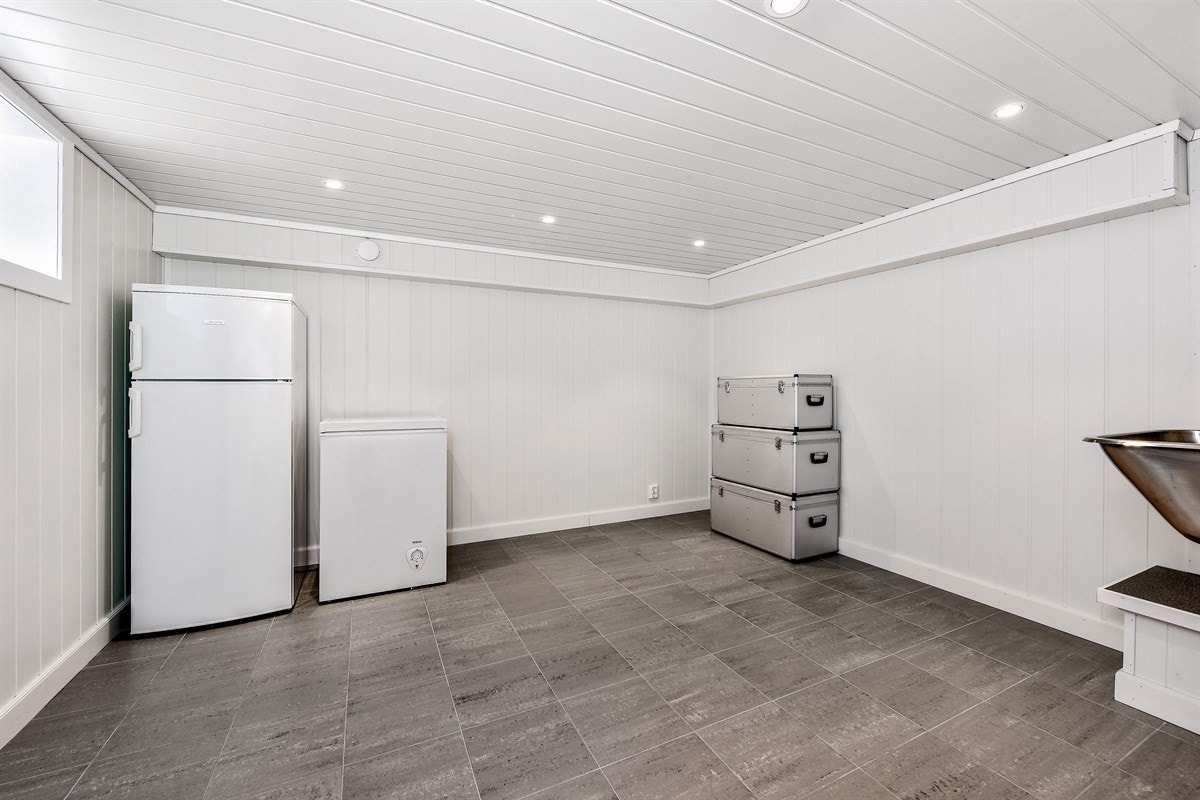 Innredningen består av vaskekum, frittstående toalett og åpent dusjhjørne. Badet har grå fliser på gulv med gulvvarme, hvite fliser på veggene og store lamper på vegg. Galleribilde