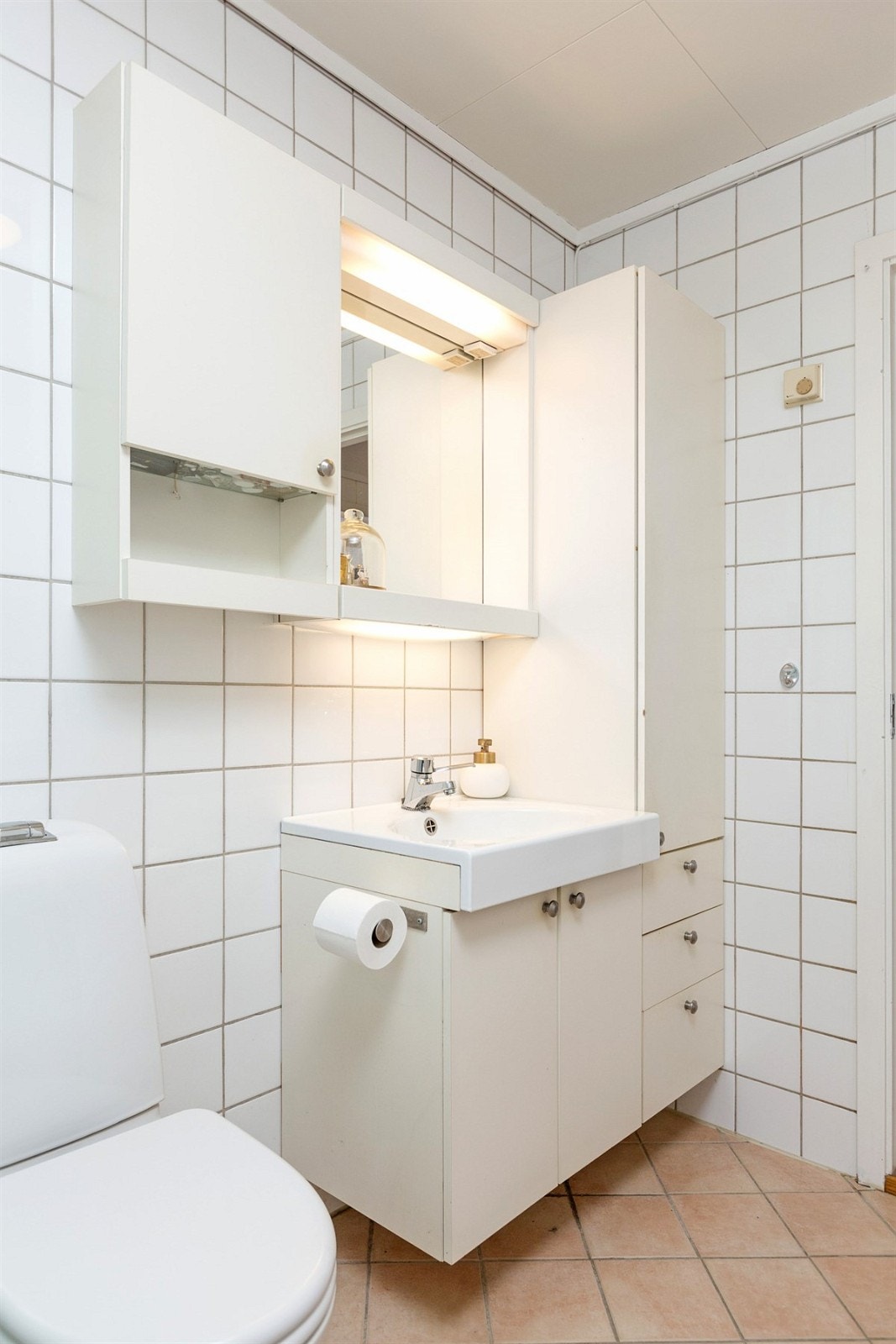 Dusjkabinett med glassdør. Nyere gulvmontert toalett. Opplegg for vaskemaskin under innredning med arbeidsbenk, underskap, overskap, og Galleribilde