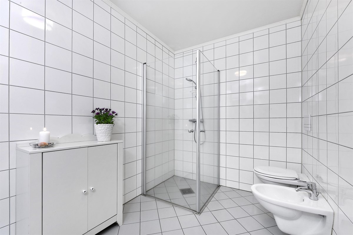Badet er innredet med et moderne, hvitt servantmøblement som har glatt skuffefront, heldekkende servant og speilskap med integrerte belysning. Galleribilde