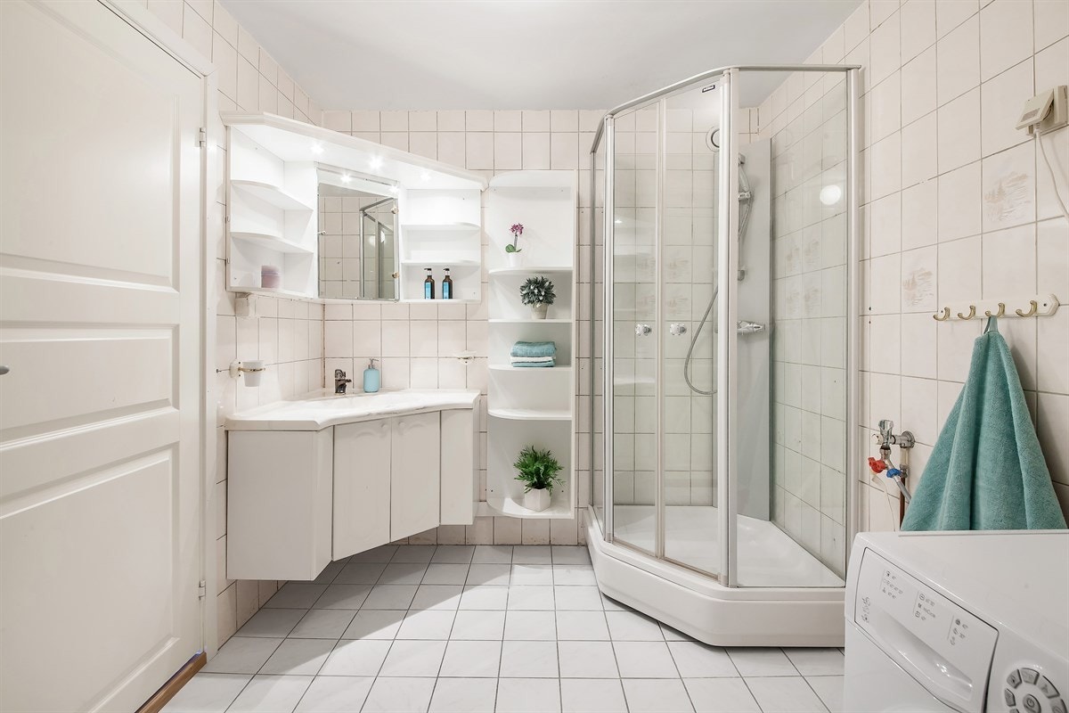 Baderommet er utstyrt med lyse fliser. Innredningen består av enkel servant nedfelt i laminert plate med hvitt underskap, speilskap med belysning og dusjkabinett Galleribilde