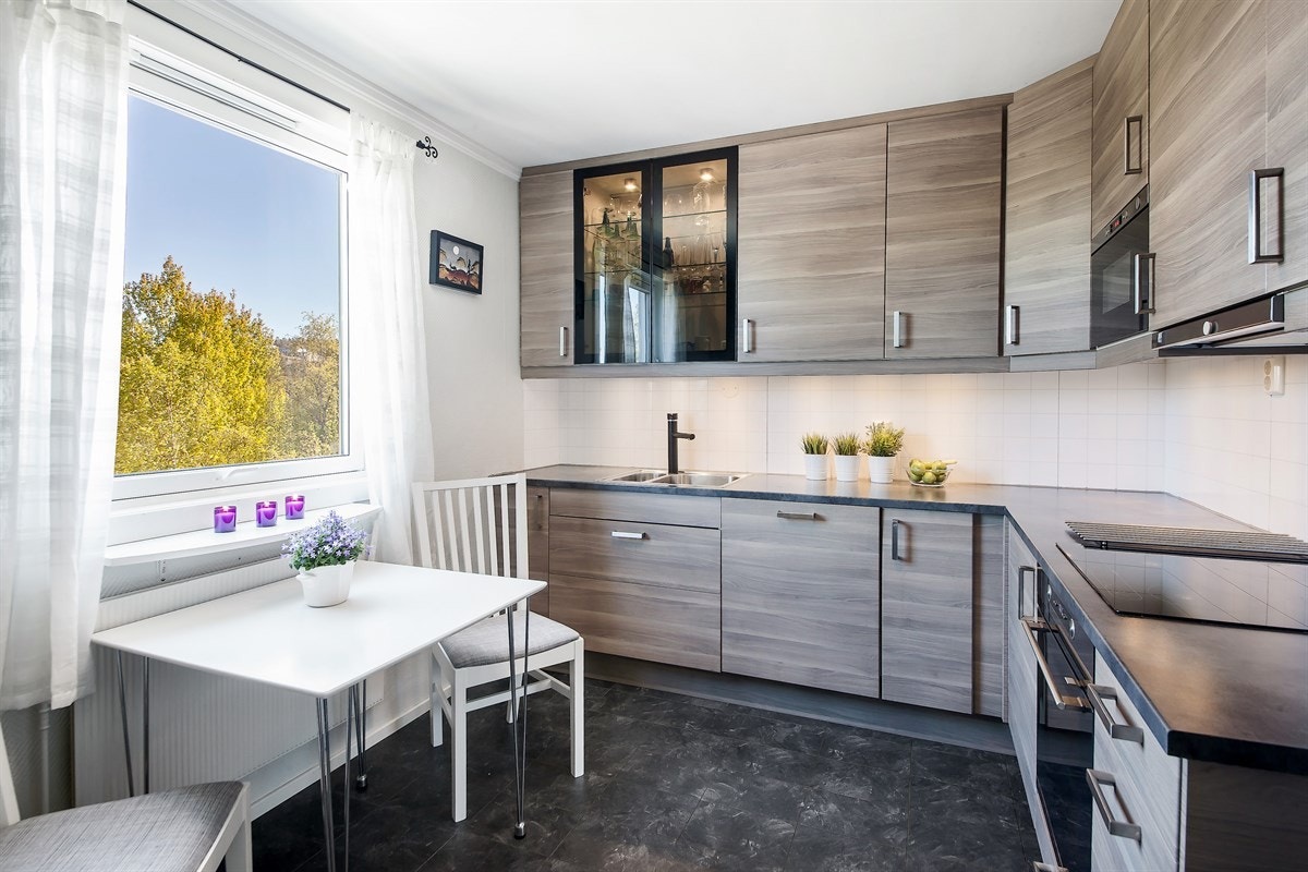 Innredningen har glatte, finerte fronter, vitrineskap, benkebelysning, lys kitchenboard og laminert benkeplate med nedfelt kum i stål Galleribilde