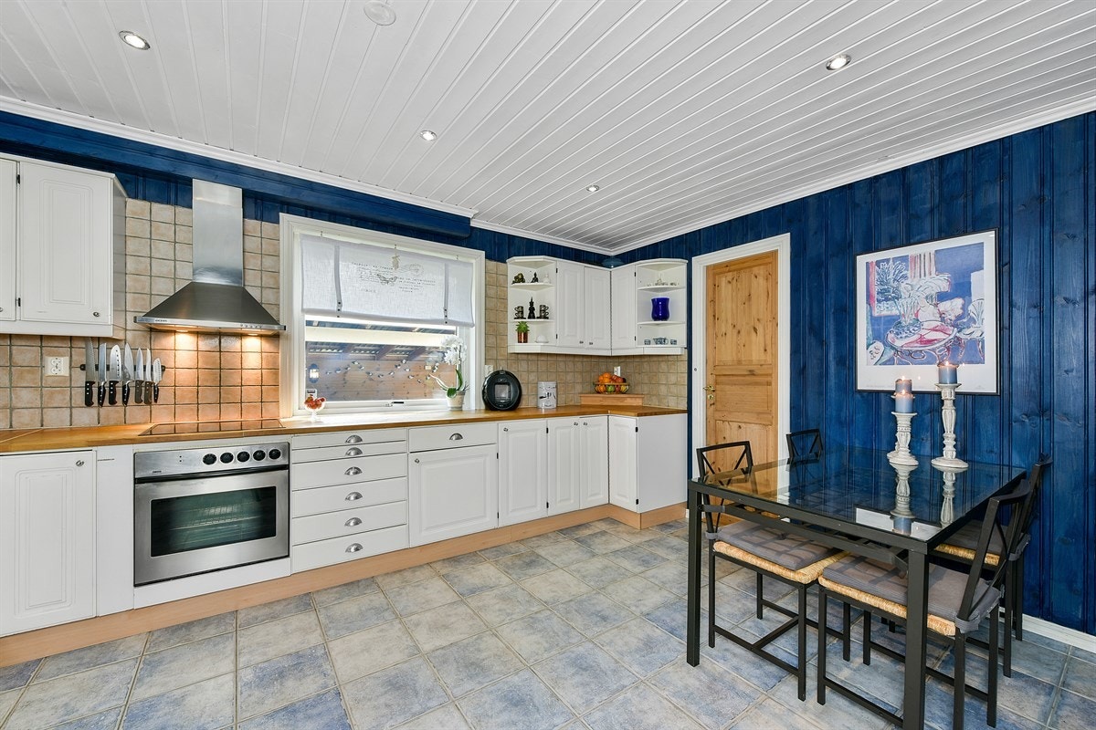 Kjøkkenet ligger i eget rom og har lyseblå fliser på gulv, blåmalt panel på veggene og downlights i lysmalt himling. Galleribilde