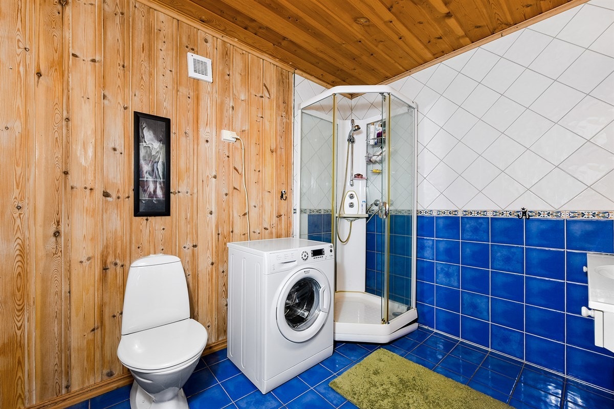 Badet har blå fliser på gulv, samt blå og lyse fliser på veggene, i kombinasjon med panel. Galleribilde