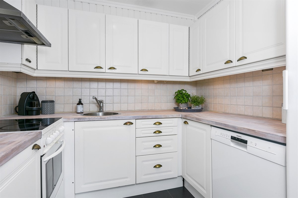 Det er fliser over benk, benkebelysning og ventilatorhette i stål over komfyrplass. Galleribilde