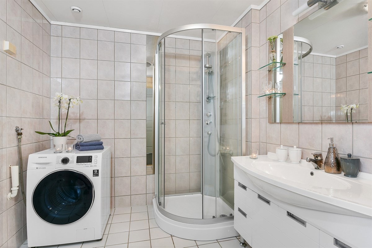 Badet ligger i første etasje og har fliser på gulv og vegger, gulvvarme, et buet dusjkabinett og opplegg for vaskemaskin. Galleribilde