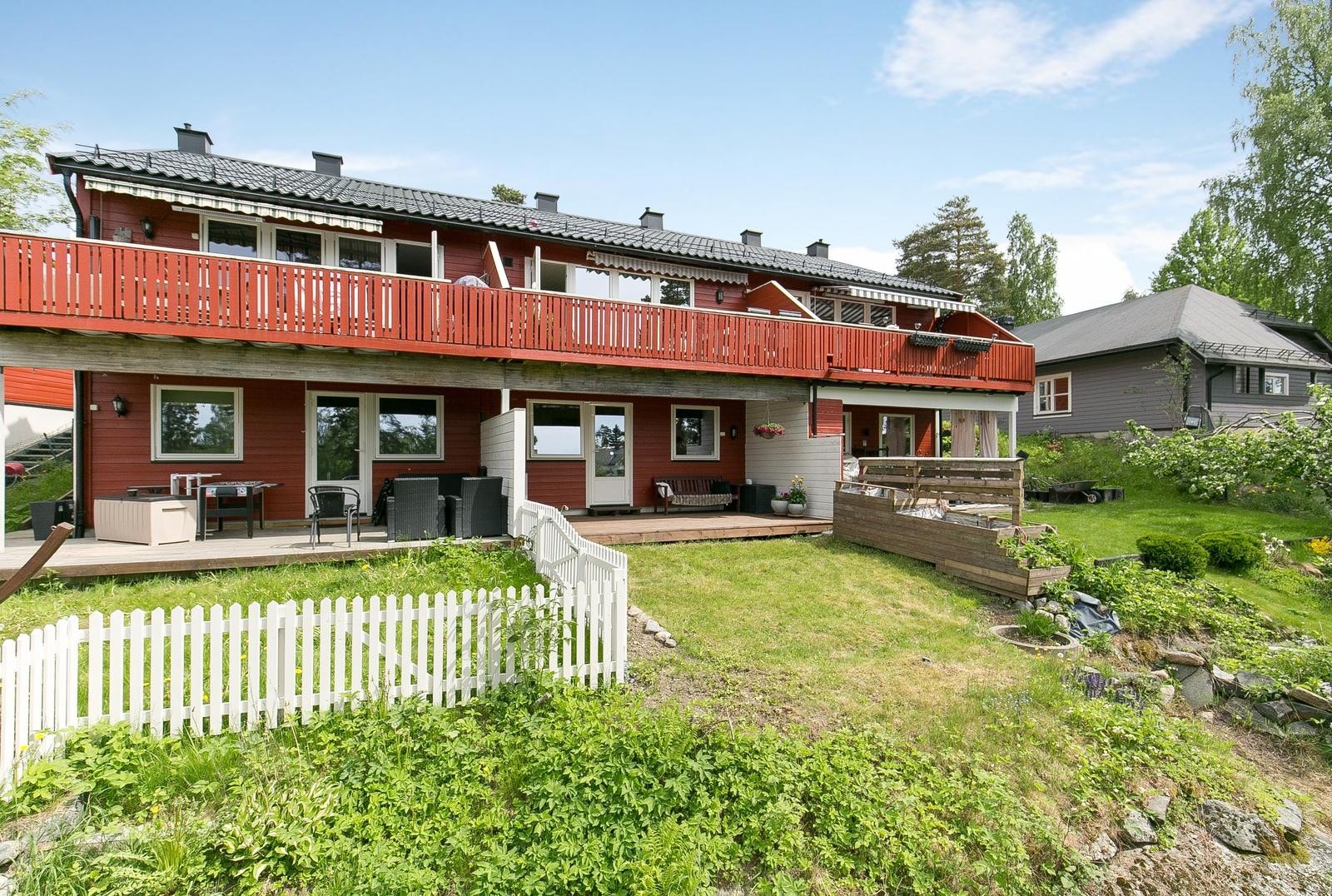 Oversikt over baksiden av rekkehuset hvor man finner terrasse, balkong og hage Galleribilde