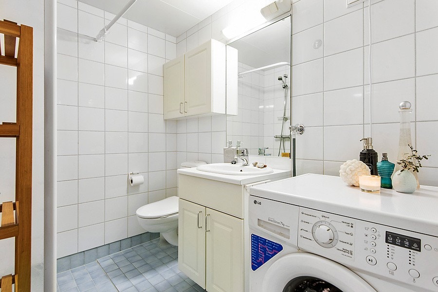 Lyst og pent flislagt bad med varmekabler i gulv og opplegg for både vaskemaskin og tørketrommel. Baderomsinnredning fra byggeår med frittstående toalett, dusjhjørne og servant med underskap . Mekanisk avtrekk i himling. Galleribilde