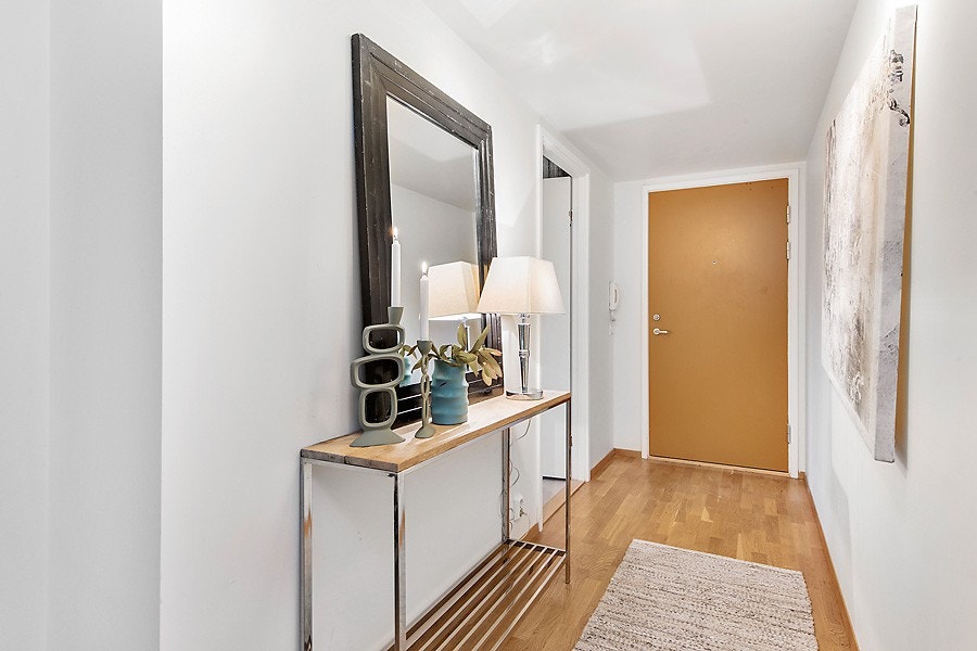 Innbydende og romslig gang. Her har du rikelig med plass for garderobeskap. 3-stav parkett på gulv og hvitmalte flater på vegg som går igjen i stuen og kjøkkenet. Galleribilde
