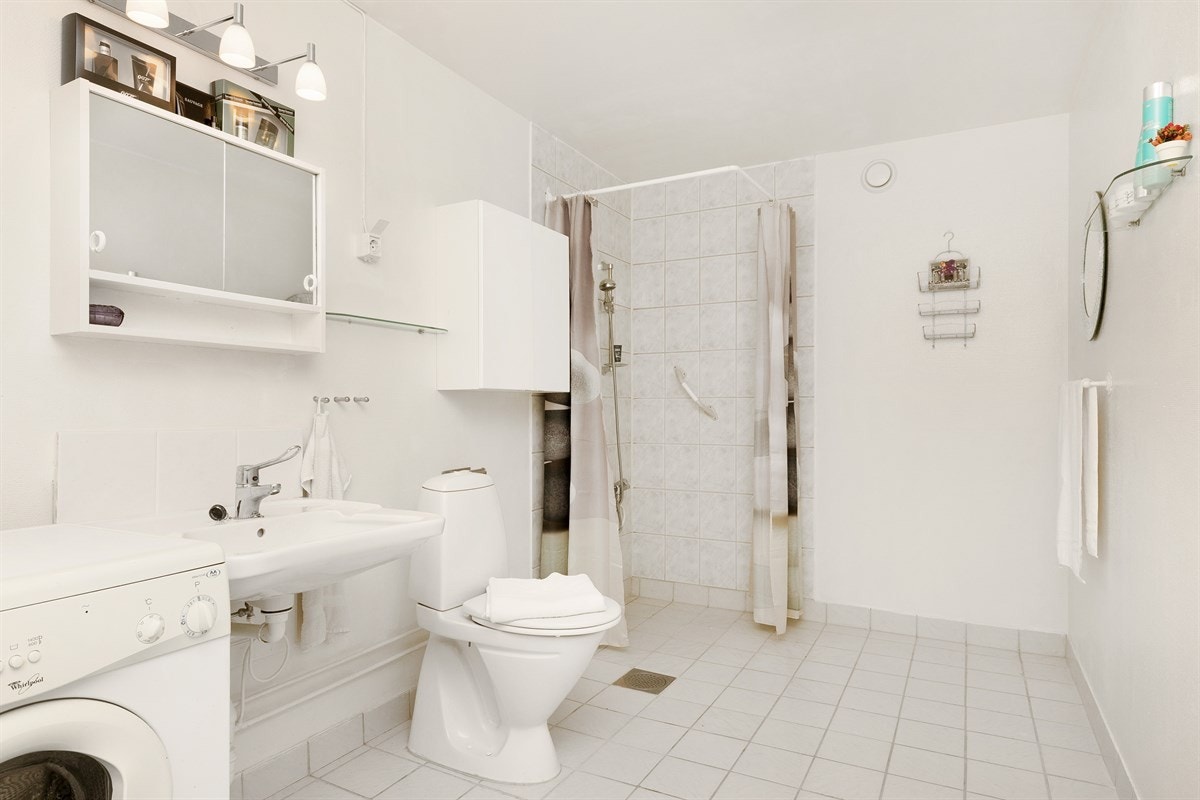 Romslig bad, flislagt gulv og flislagt i dusjsone. Servant, toalett, dusjhjørne. Opplegg for vaskemaskin. Galleribilde