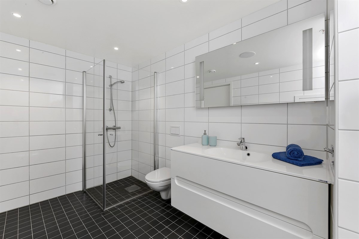 Hovedbadet har bred servant med hvite skuffer, speil med integrert belysning og dusjhjørne med rette, innfellbare glassdører. Galleribilde