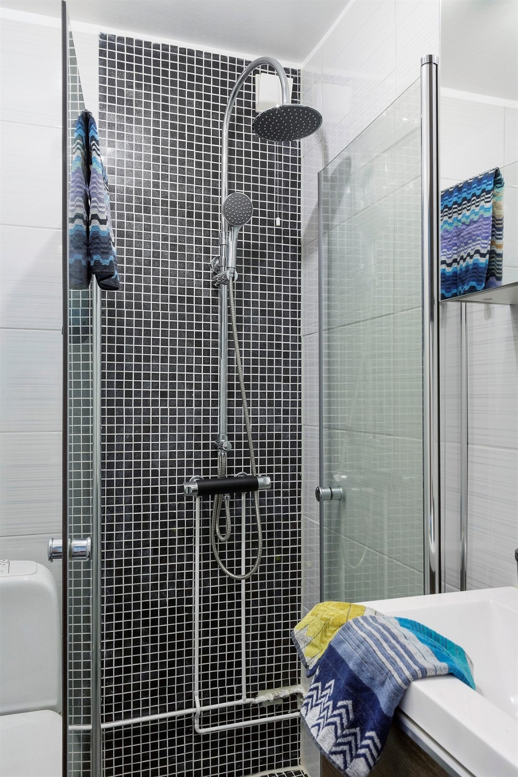 Delikat flislagt bad med rainshower, servant med innredning, speilskap og design kran. Galleribilde