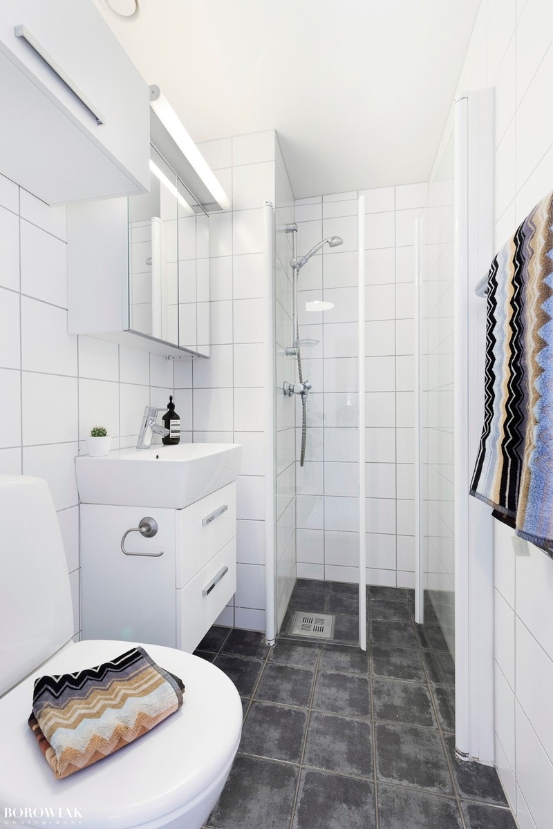 Badet har en praktisk dusjnisjè adskilt fra resten av badet med doble innfellbare glassdører. Stilige mørke fliser på gulv og lyse fliser på vegg i tidsmessig utførelse Galleribilde
