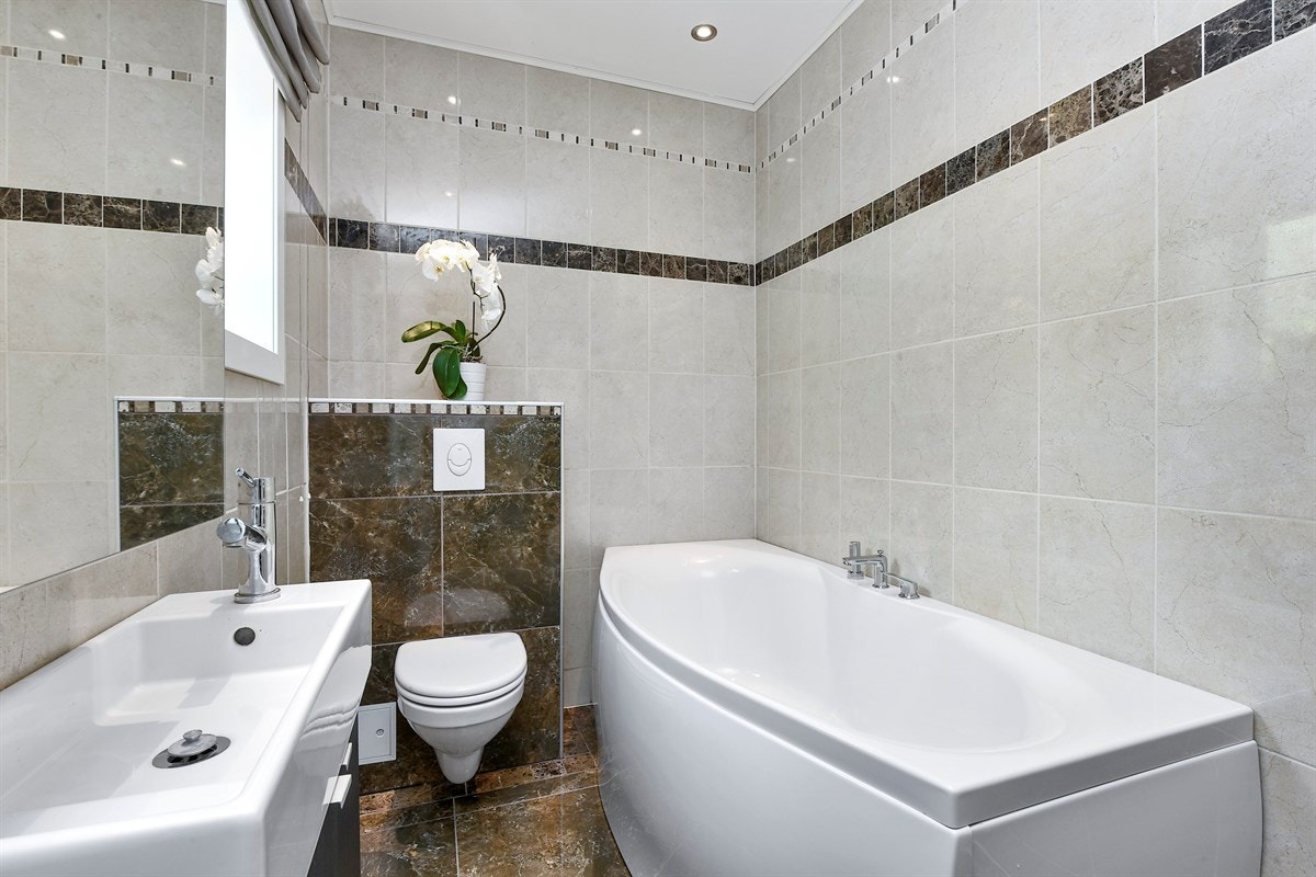 Det andre badet er holdt i samme stil, med marmormønstrede fliser på gulv og sisternekasse, lyse veggfliser, pene dekorborder, gulvvarme og downlights belysning. Galleribilde