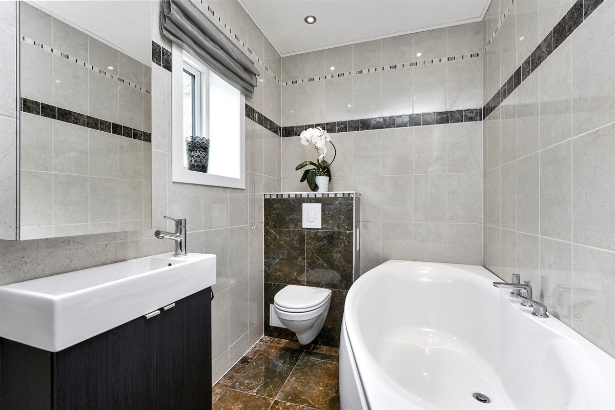 Innredningen består av servant på mørkt servantskap, speilskap, veggmontert toalett og et delikat badekar. Galleribilde