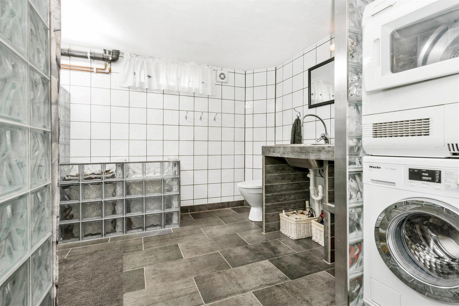 Det romslige vaskerommet/baderommet i kjelleren med fliser på gulv med elektriske varmekabler. Galleribilde