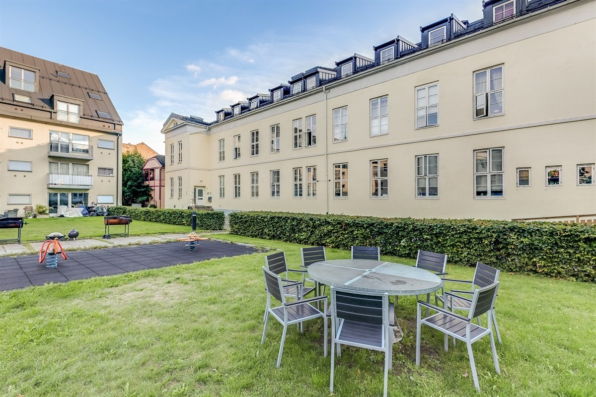Pent opparbeidet fellesareal med sitteplasser, plen og beplantning. Galleribilde
