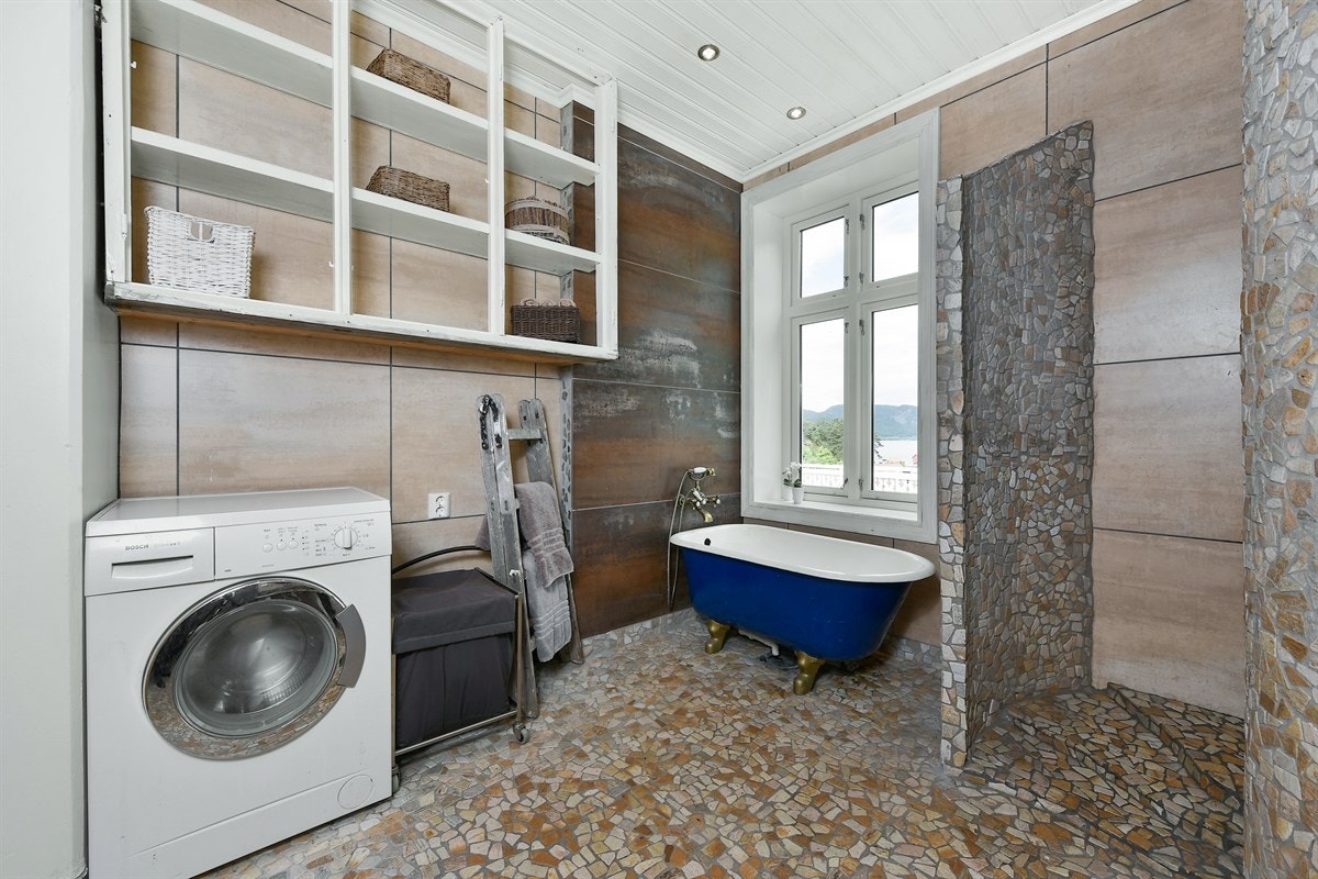 Under vinduet er det plassert et badekar i blå emalje med løveføtter og armatur i messing. Galleribilde