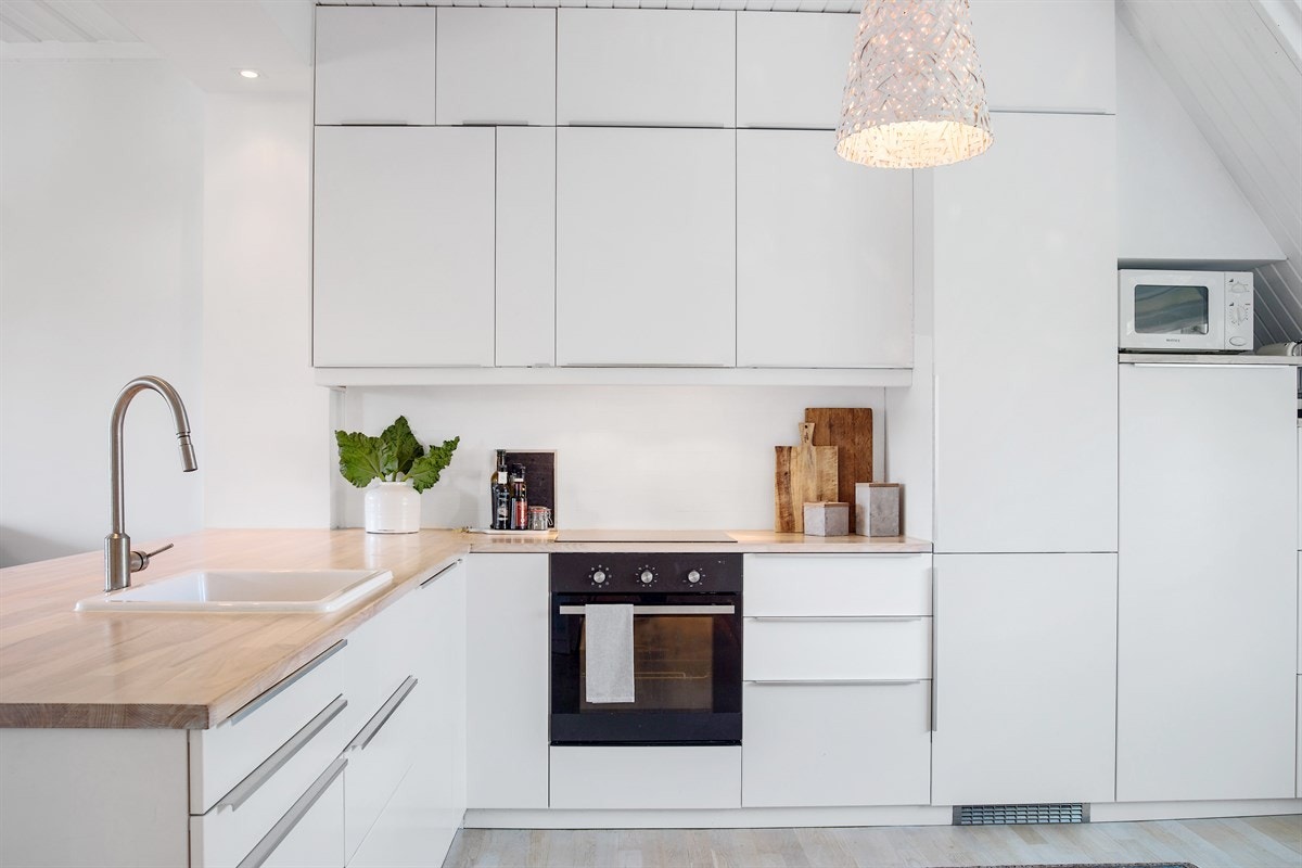 Innredningen er stilren og moderne med hvite, håndtaksløse fronter, hvitmalt hylle, lyslister, hvite fliser og benkeplater i heltre eik. Galleribilde