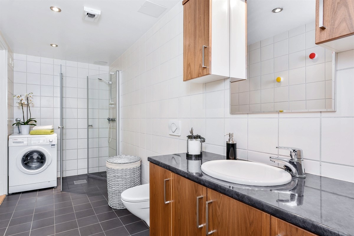 Badet har veggmontert toalett og dusjhjørne med innfellbare glassdører. Galleribilde