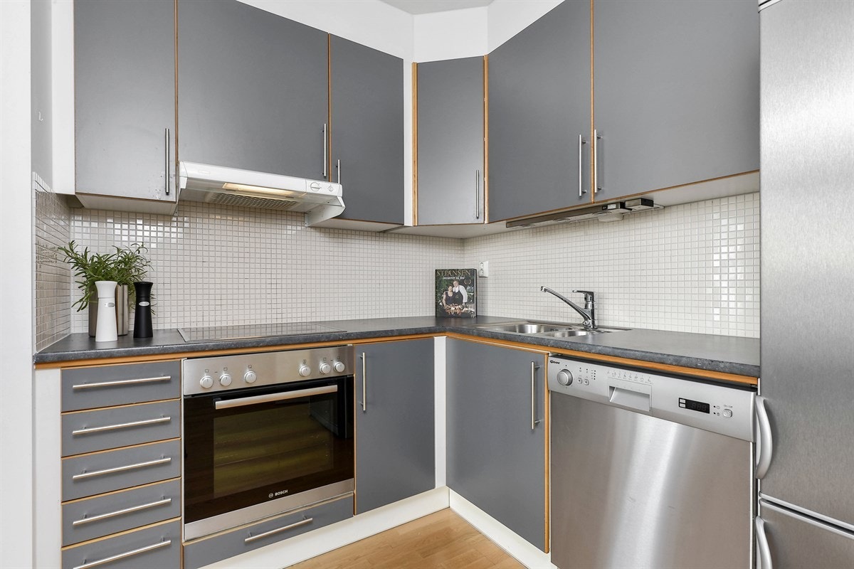 Over benken er det fliser og belysning. Kjøkkenet er utstyrt med hvitevarer i form av integrert stekeovn, keramisk topp og oppvaskmaskin og et kjøleskap i nisje. Galleribilde