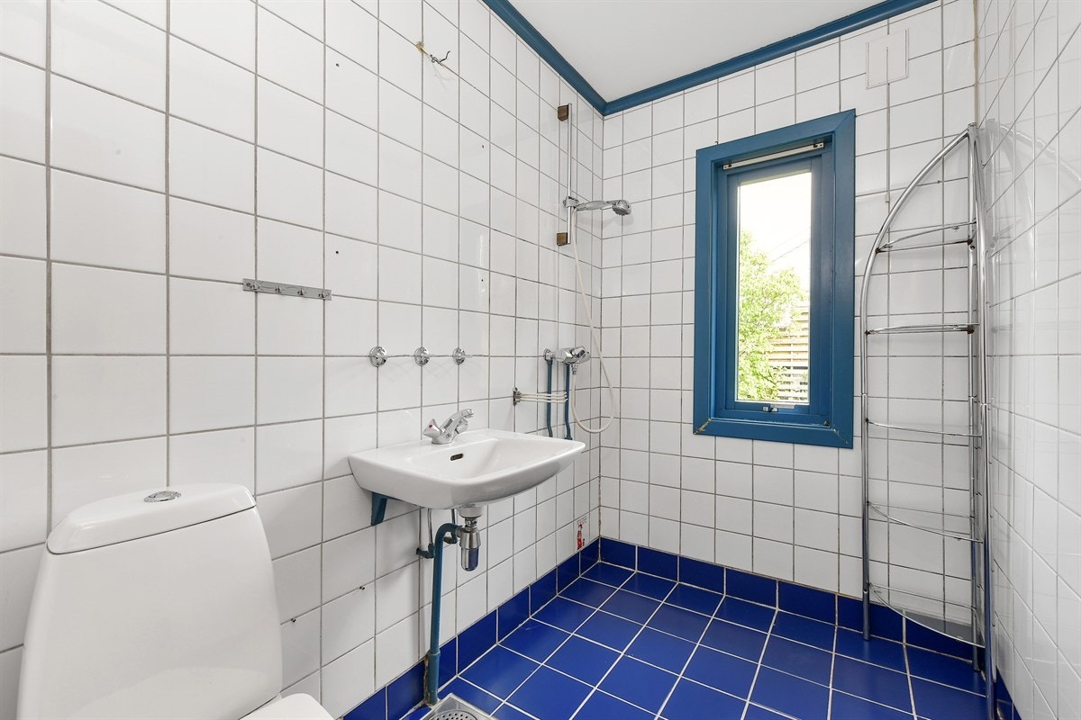 Badet i første etasje har koboltblå fliser på gulv, hvite fliser på veggene og et vindu som gir dagslys. Galleribilde