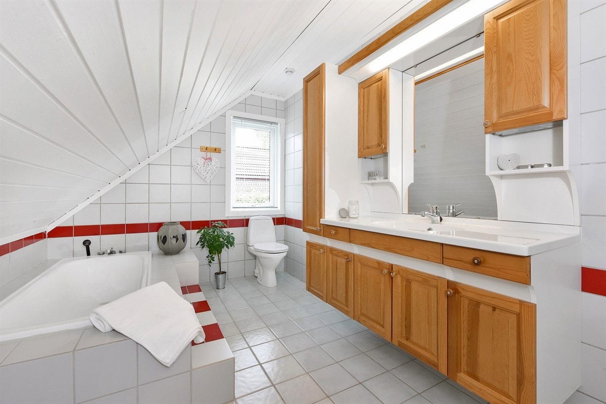 Badet er utstyrt med et frittstående toalett og et innfliset badekar. Opp til badekaret er det murt et trappetrinn som er flislagt og hvor de røde veggdetaljene er tatt igjen. Galleribilde