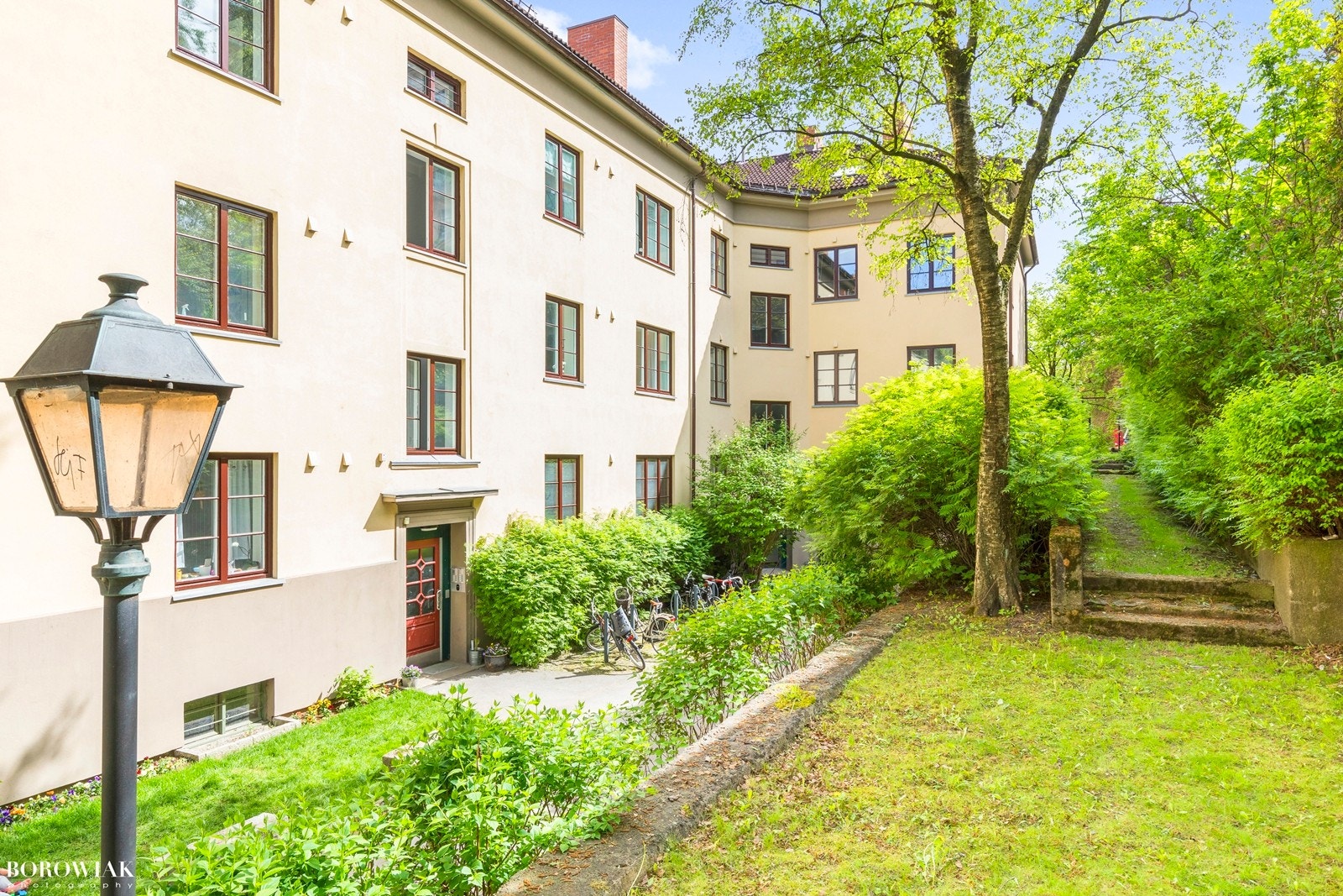 Pent opparbeidet fellesareal med plen og beplantning med bl.a. asfaltert internvei med lampebelysning, plen og trær. Galleribilde