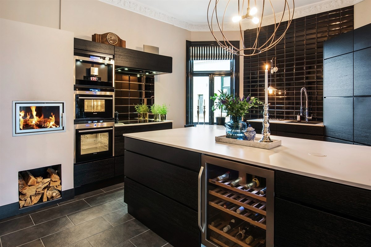 Innredning med sorte finerte fronter, komposittlaminat benkeplater med underlimt kum. Integrert oppvaskmaskin, stekeovn, induksjonstopp (80 cm), dampovn, kaffemaskin, vinskap, 2 kjøleskap og 2 fryseskap Galleribilde