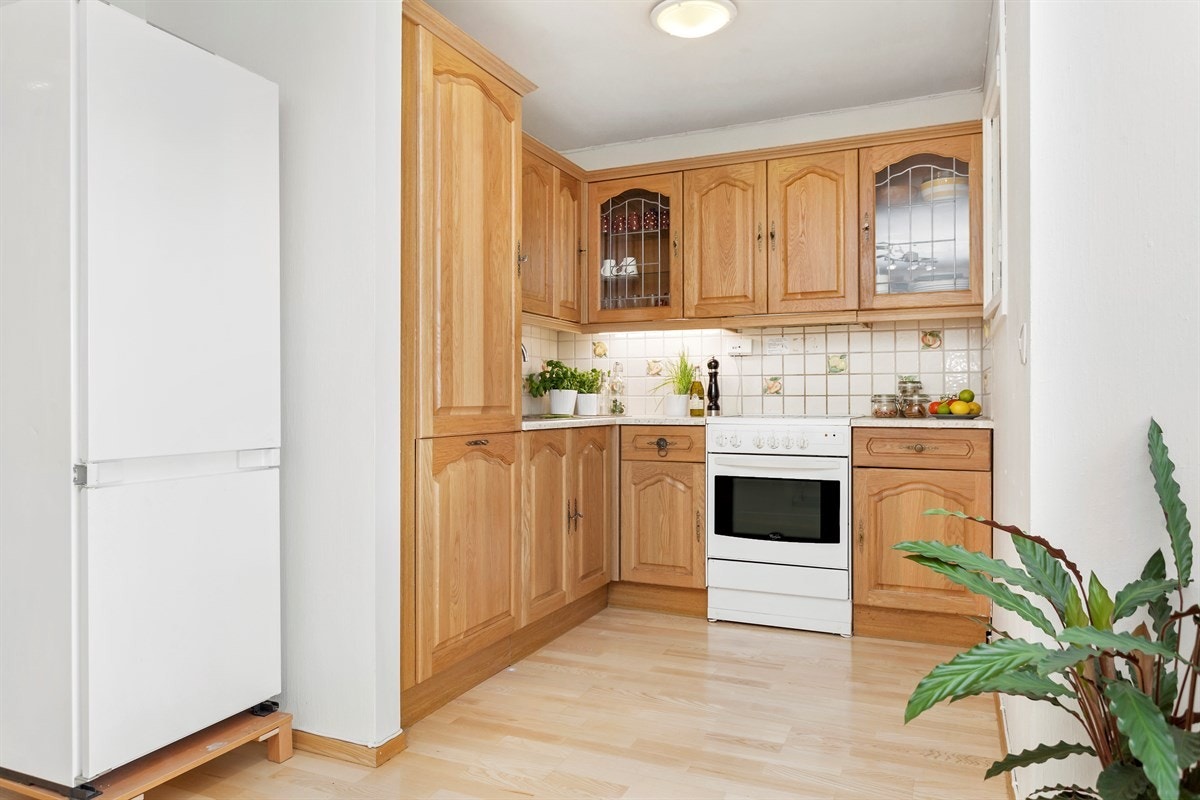 Kjøkkeninnredning med eikefronter, dobbel oppvaskkum, ettgrepskran, laminert benkeplate, overskap med 2 vitrinedører, ny integrert oppvaskmaskin og ventilator med kullfilter. Galleribilde