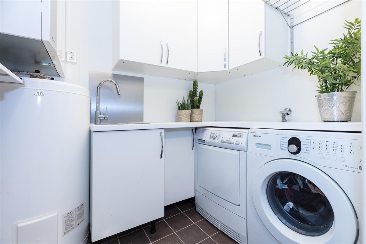 Familievennlig vaskerom/teknisk rom med flislagt gulv med gulvvarme og våtromsplater på overflater. Boligens varmtvannsbereder på ca. 194 liter er plassert her, samt sentralstøvsuger, og boligens balanserte ventilasjonsanlegg med varme-gjenvinner. Galleribilde